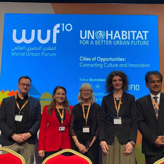 secretária Patrícia Macedo em pé posando para foto ao lado de duas mulheres e dois homem em frente a painel com nome do evento